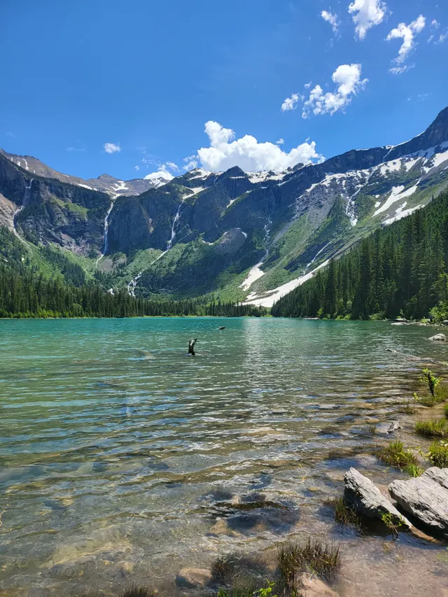 Clear turquoise lake below steep mountains in Glacier